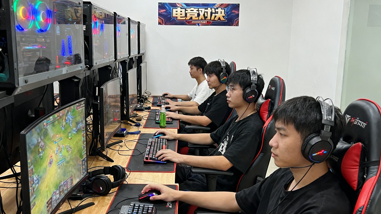 某互联网公司团建电竞赛现场，办公室被临时改造为五人对战区，员工们坐在高性能电脑前全神贯注地进行王者荣耀比赛